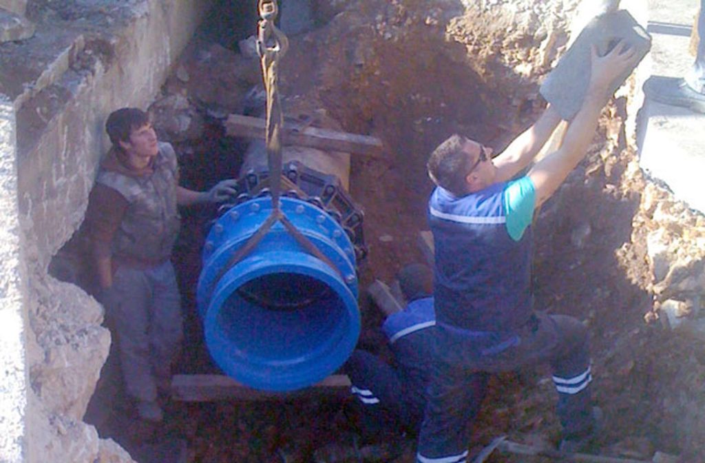 Workers installing a large blue pipe inside a trench
