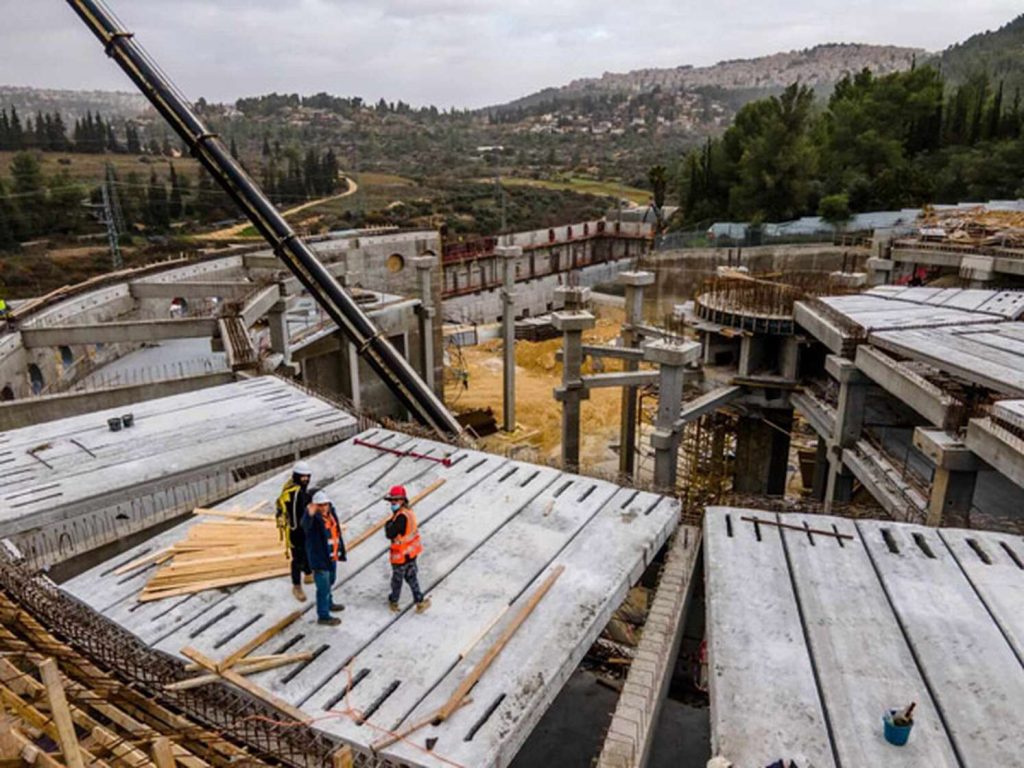 Three construction workers in hard hats standing on a concrete slab at a hillside construction site