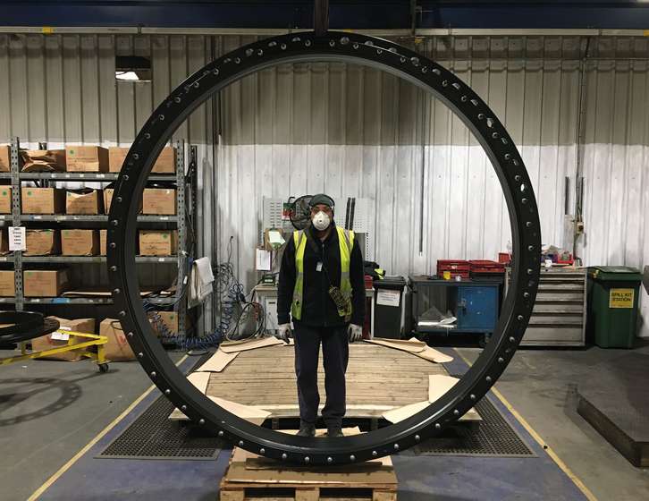 A factory worker wearing protective gear framed inside a large circular metal ring