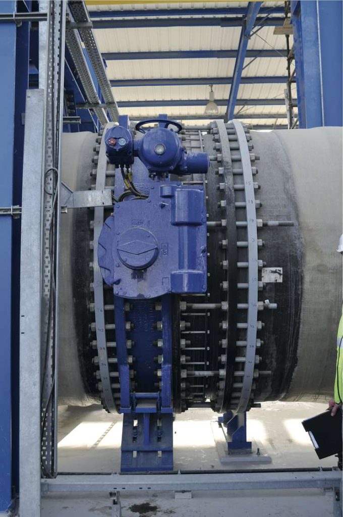 Large blue industrial valve with an actuator mounted on a large pipeline inside an industrial facility