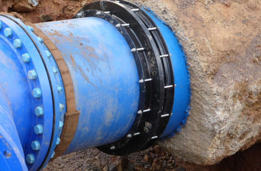 Large blue water pipe with a black bolted flange coupling entering a concrete wall