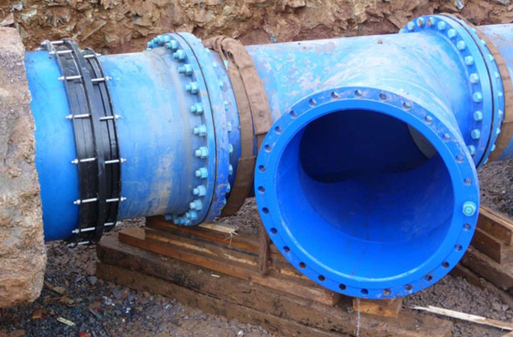Large blue flanged T-piece water pipe with bolted joints installed in a trench