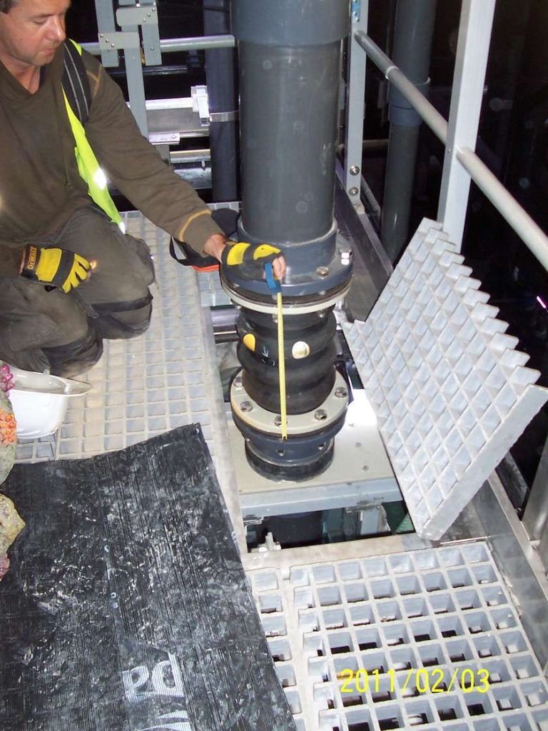 A technician using a tape measure to check a flexible rubber joint on a vertical industrial pipe
