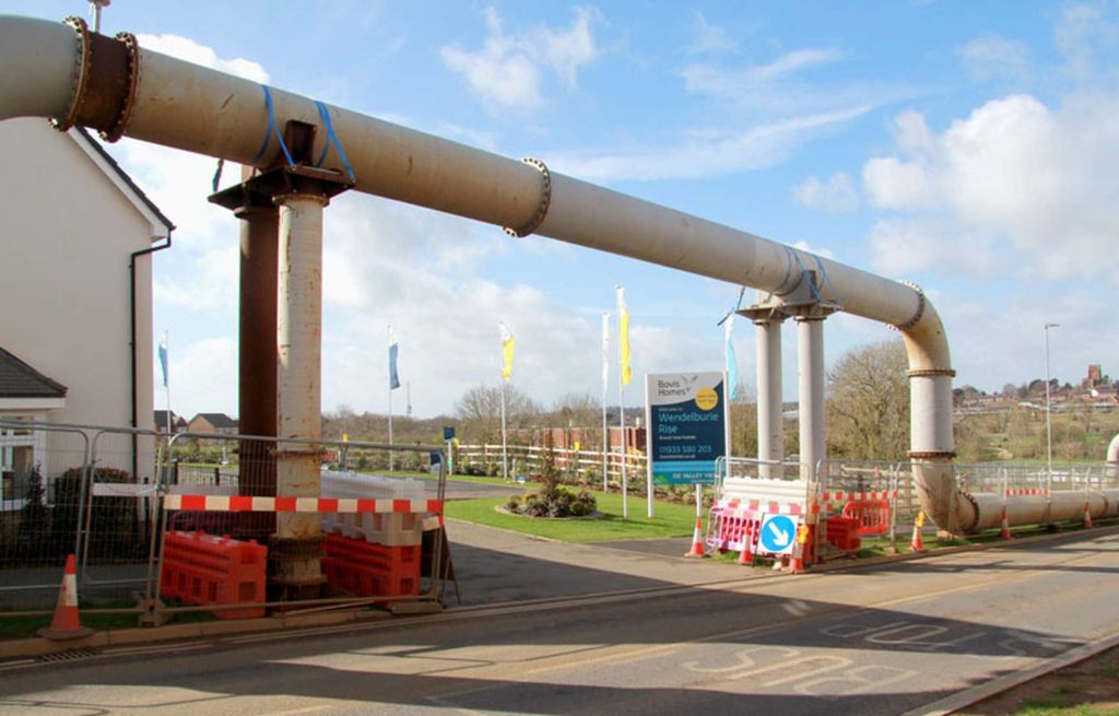 A large elevated pipe spanning across a road at a housing development site