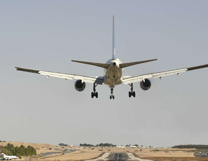 Rear view of an aeroplane descending towards a runway with landing gear deployed