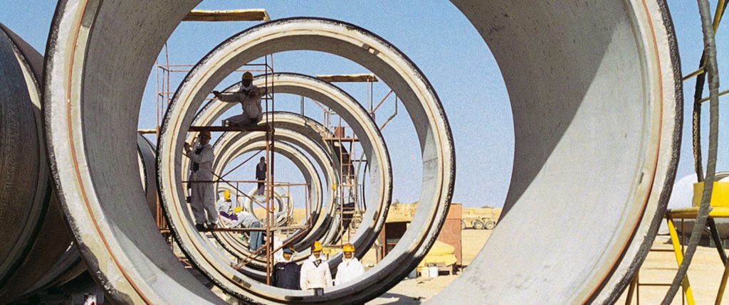 Construction workers in hard hats working on scaffolding inside massive concrete pipes on a desert site