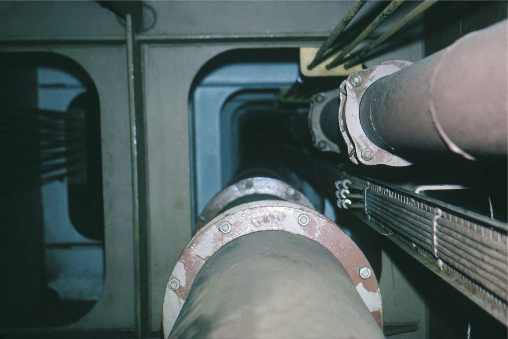Large pipes with flanged joints and cables running through a dark industrial utility shaft