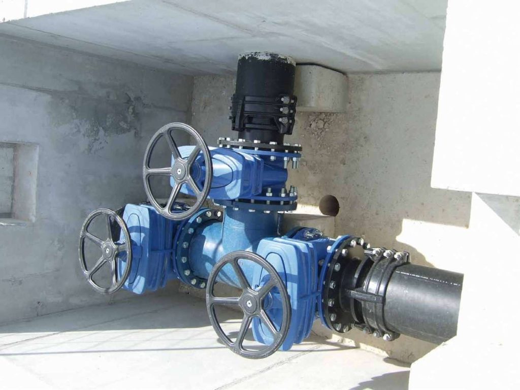 Blue industrial valve assembly with three handwheels inside a concrete chamber