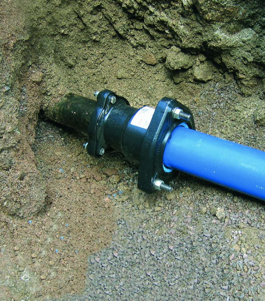 A blue pipe connected to a black pipe using a bolted mechanical coupling in a trench