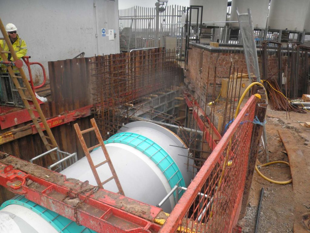 Large cylindrical pipe section installed inside a shored excavation trench at a construction site surrounded by rebar