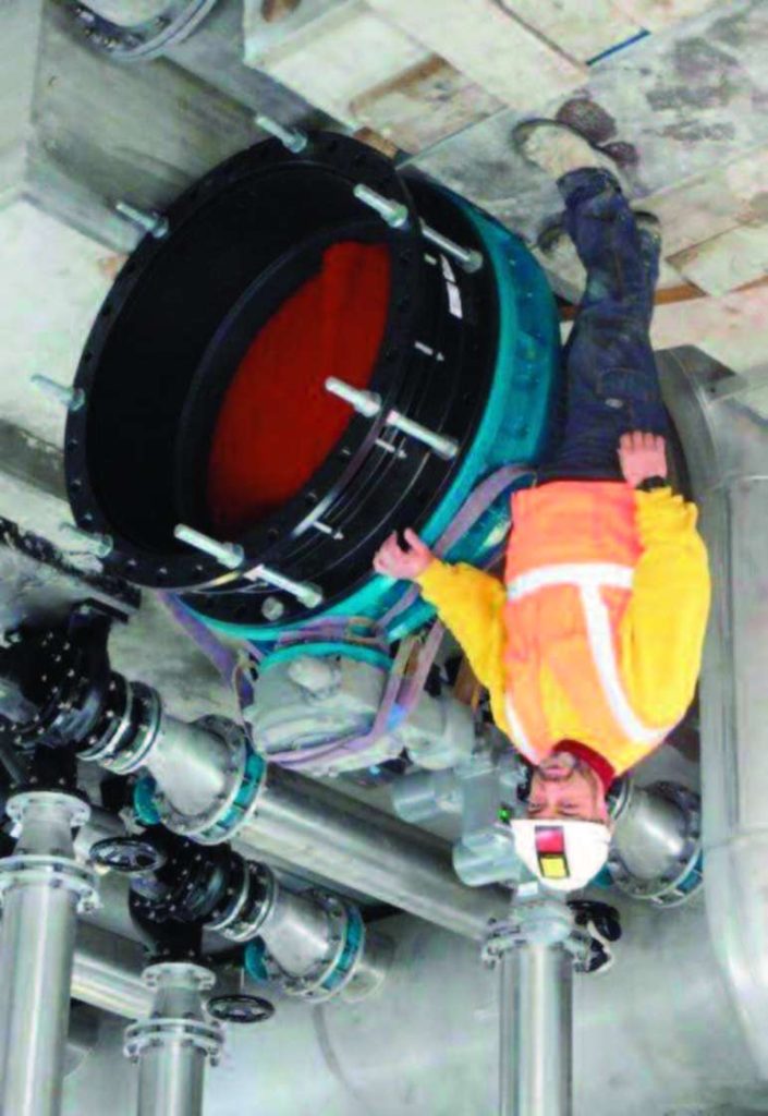 A worker in a high-visibility jacket and hard hat standing beside a large industrial pipe valve