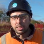 Construction worker wearing a black hard hat, safety glasses, and high-visibility vest