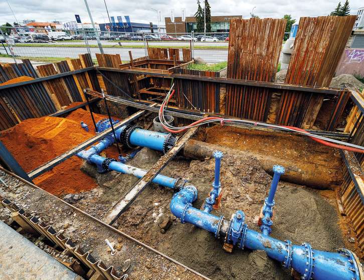 An open excavation trench reinforced with sheet piling, showing installed blue water pipes and valves