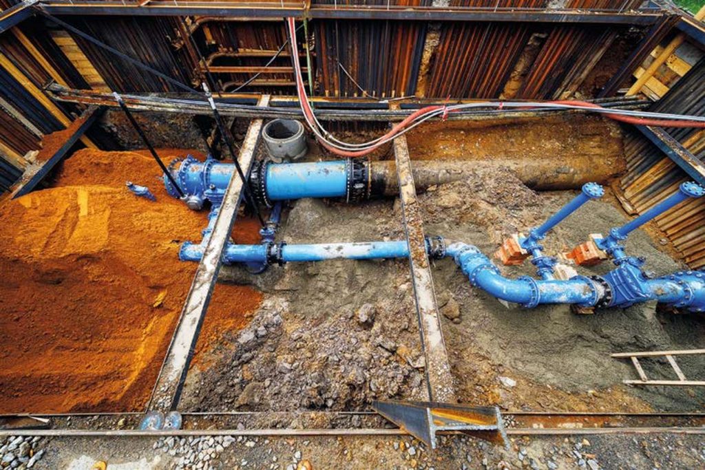 Large blue water pipes installed inside an excavated construction trench with steel shoring
