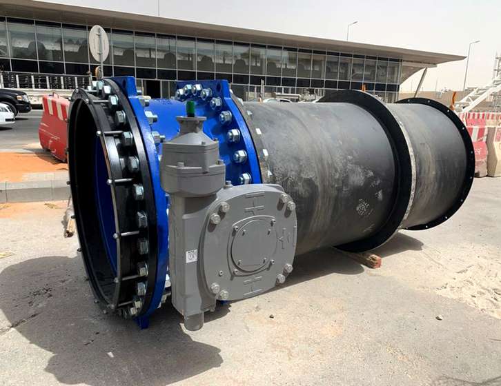 Large industrial pipe assembly with a blue flanged valve and grey gearbox actuator resting outdoors