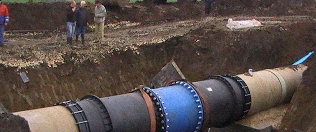 Workers standing at the edge of a deep trench where a large industrial pipeline is being installed