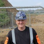 Smiling construction worker wearing a patterned Farrans hard hat at a construction site