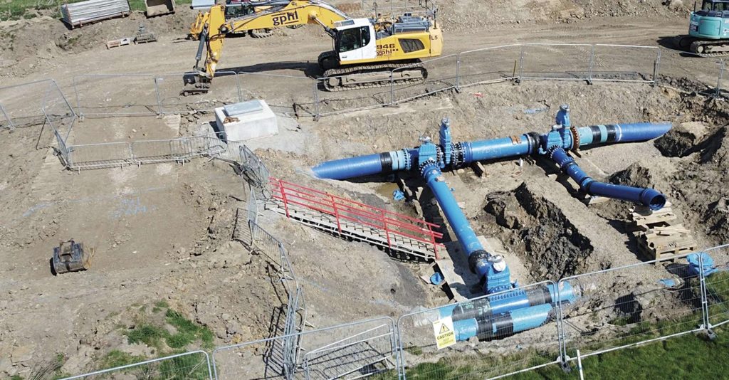Aerial view of large blue water pipes and valves installed in an excavated trench on a construction site
