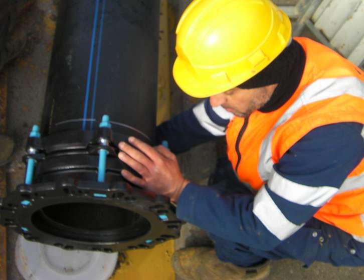 A worker in a yellow hard hat and high-visibility vest fitting a flange adaptor onto a large black pipe