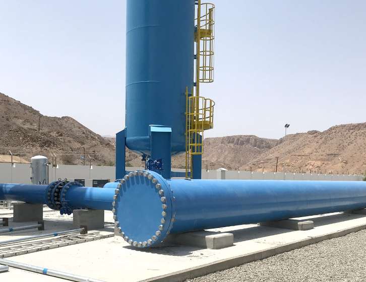 Large blue industrial vertical tank and heavy pipeline with yellow ladder in a desert landscape