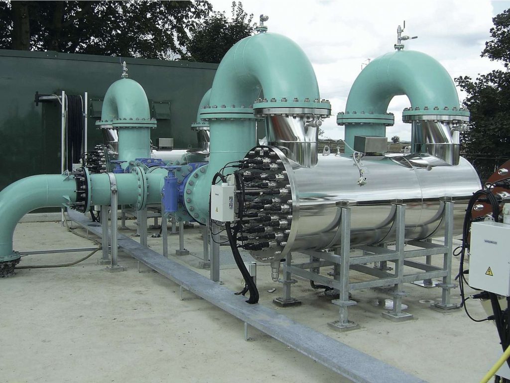 Industrial water treatment equipment featuring large stainless steel cylinders connected to curved mint green pipes