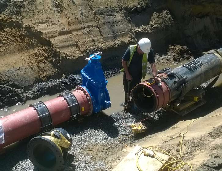 A construction worker inspecting a large blue valve on an underground pipeline in a trench