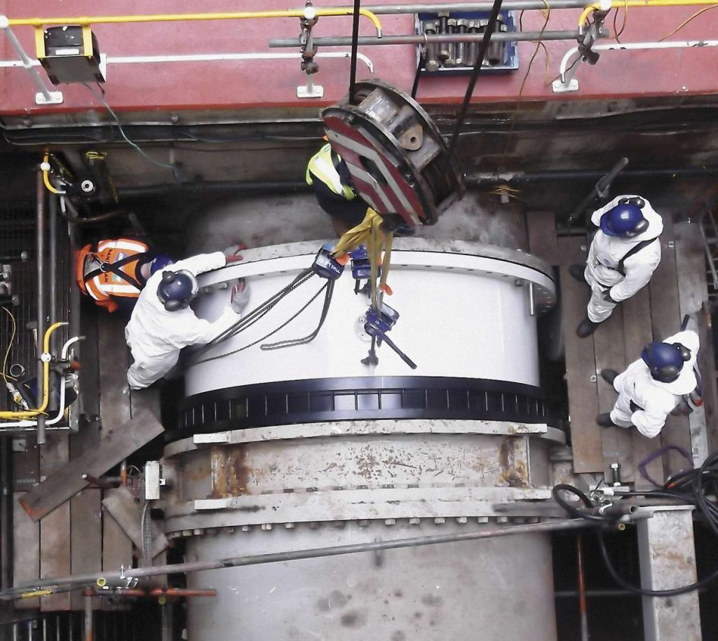 Overhead view of workers in protective gear guiding a large industrial pipe hoisted by a crane